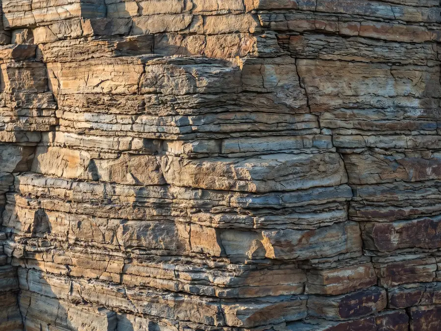 Layered sedimentary rock face in warm afternoon light, each horizontal band built on the one below